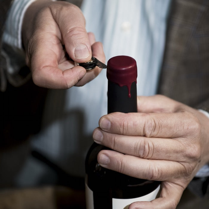 vue proche sur des main d'homme age en train d'ouvrir une bouteille de vin rouge avec sur le goulot de la cire rouge 