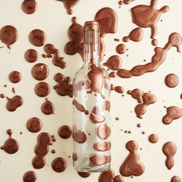 Bouteille en verre ciré de cire dure cuivre métallisée luisante avec des tache de cire cuivré en fond. 