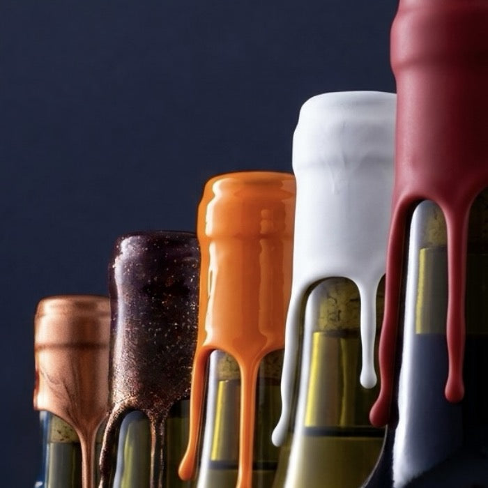 alignement de plusieurs bouteille avec toutes un goulot de cire différentes : rouge souple, blanc souple, orange dure, lie de vin pailletté, et cuivre métallisé. 