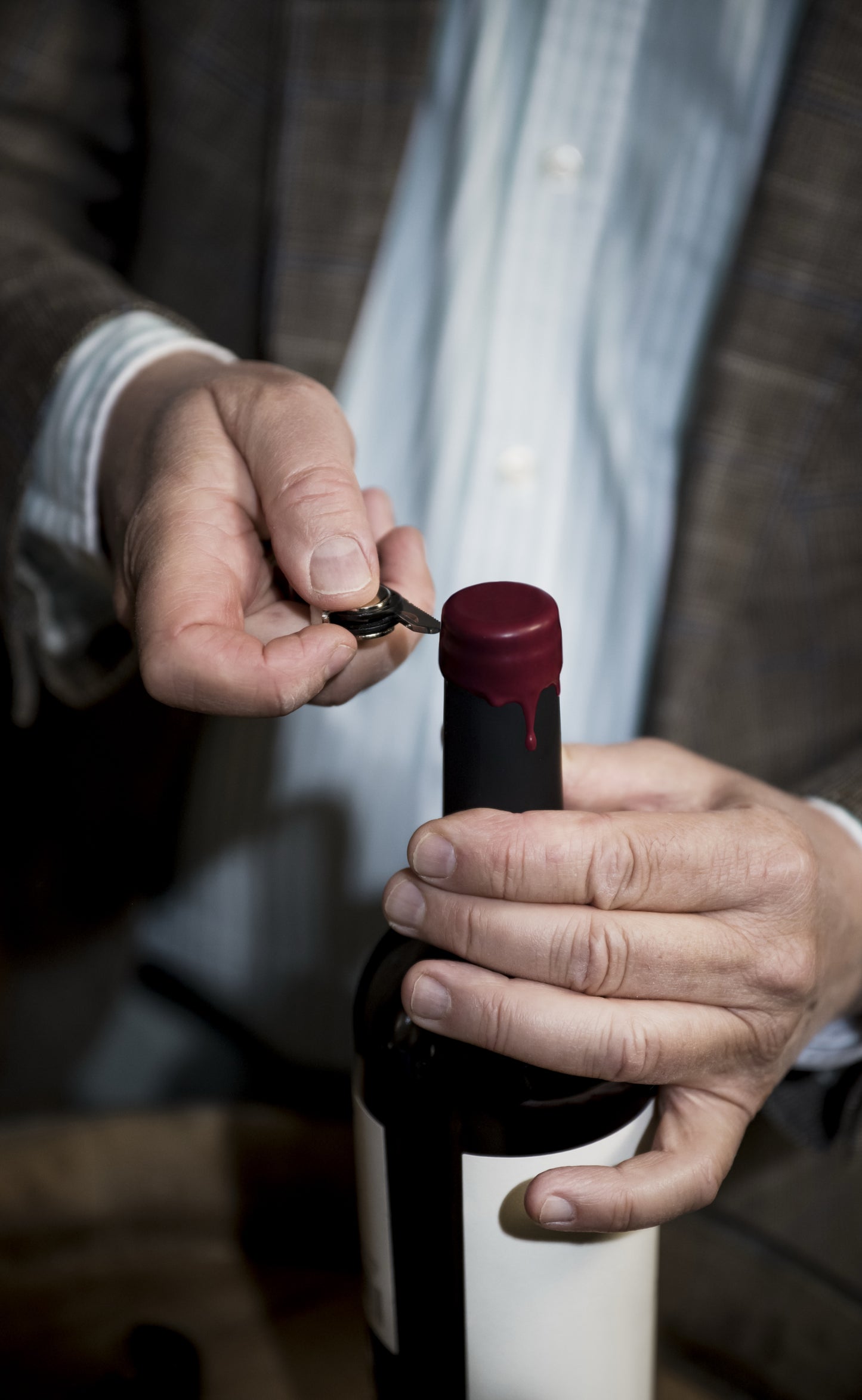 vue sur des main d'homme age en train d'ouvrir une bouteille de vin rouge avec sur le goulot de la cire rouge 