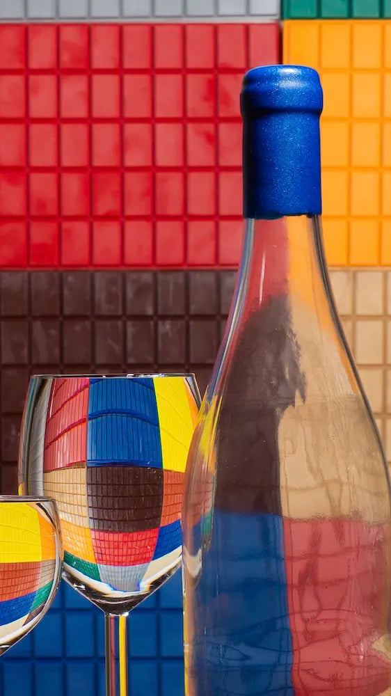 A l'arriére des plaques de cire collés au mur de multiple couleurs, avec en avant une bouteille transparente de cire bleu et un verre avec de l'eau. 